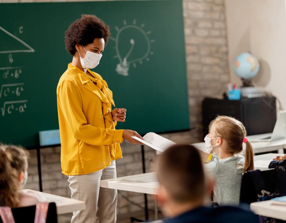 A teacher wearing a mask and interacting with a student